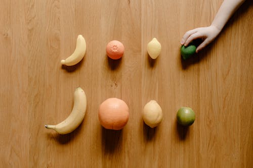 Anonymous kid near citruses and bananas on wooden floor