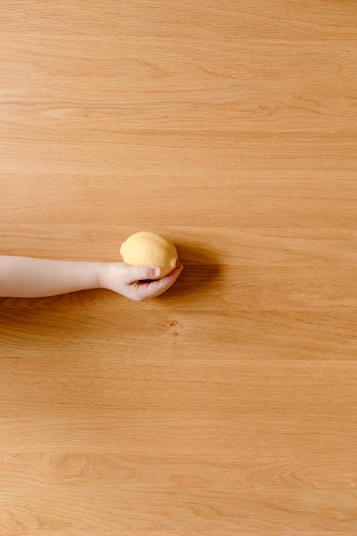 Faceless kid with lemon in hand on wooden floor