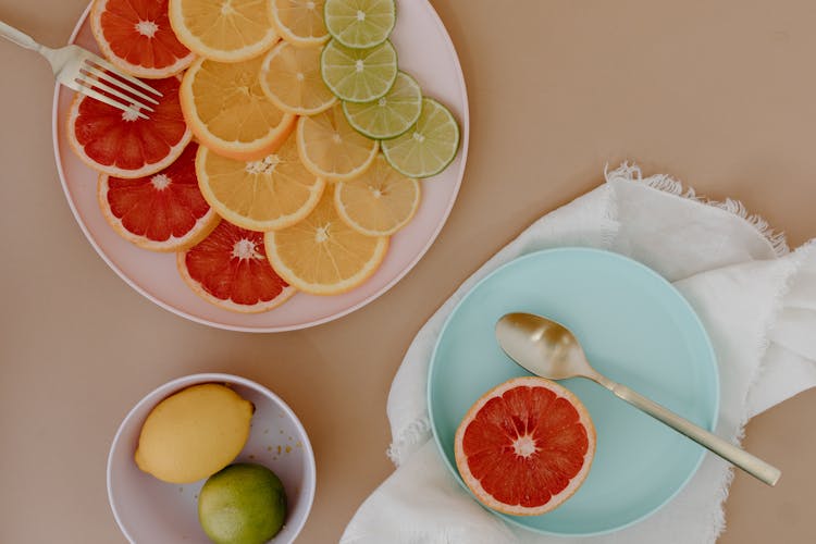 Plates With Sliced Citrus Fruits With Cutlery Near Bowl