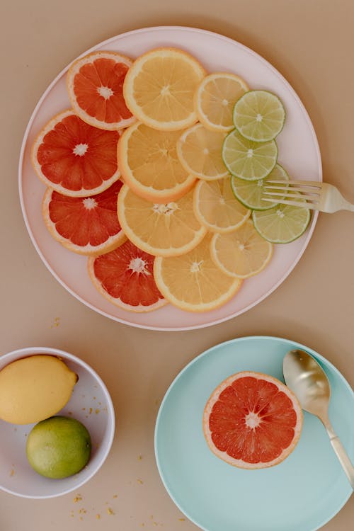 Sliced citrus fruits on plates with cutlery near bowl