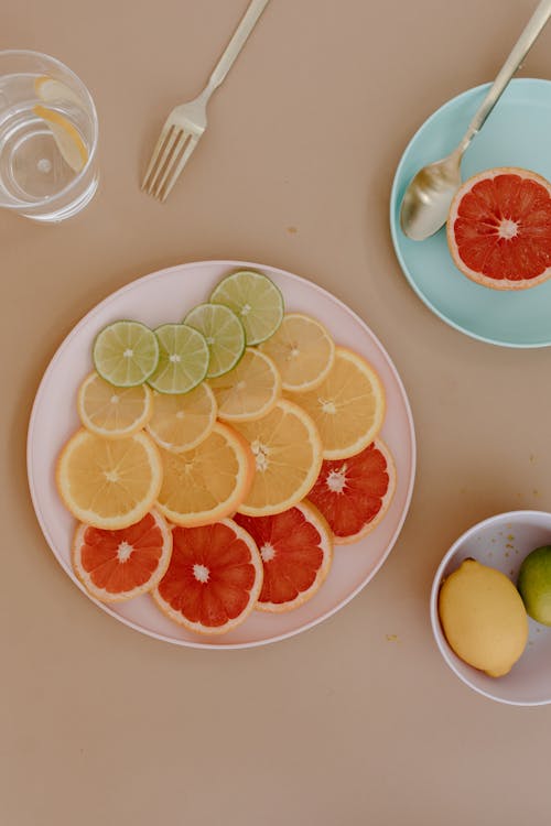 Plates with citrus fruits near cutlery and bowl near glass