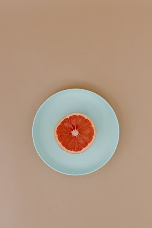 Top view of sliced red ripe grapefruit on ceramic plate on beige surface in light place