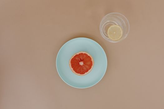 Top view of sliced red grapefruit on ceramic plate near glass bowl with sliced yellow lemon in water on beige surface in light place