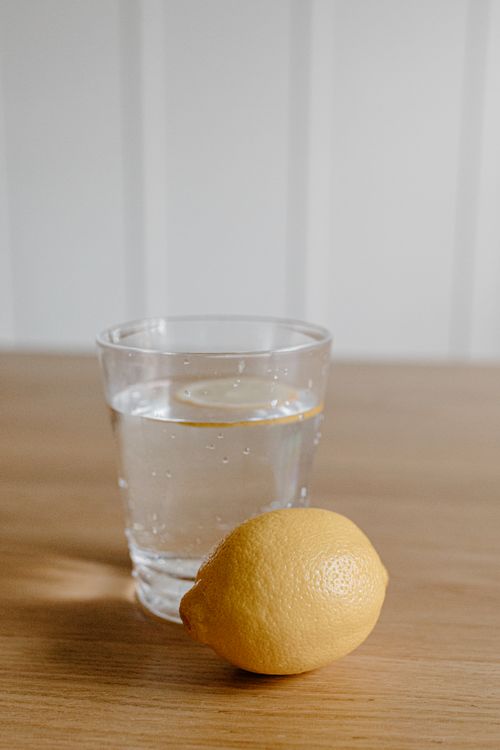 Free A clear glass of water with a lemon slice on a wooden table under soft indoor lighting. Stock Photo