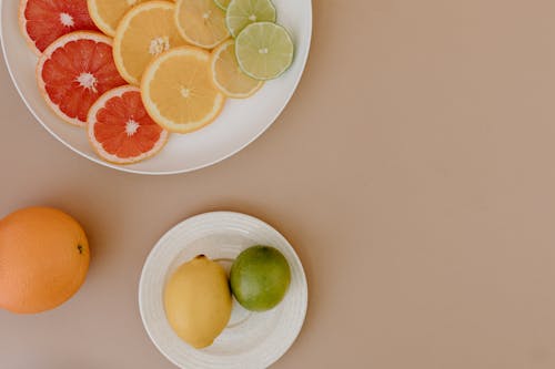 Top view of sliced red grapefruits with oranges near yellow lemons and green limes on plates on beige surface in light place