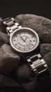 Black and white from above of shiny silver wristwatch with white clock face placed on pile of rough stones