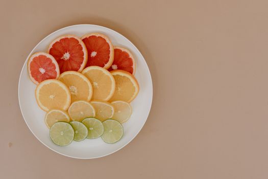 Top view of plate with sliced oranges and green limes near red grapefruits and yellow lemons on beige surface in light studio