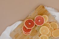 Top view of wooden cutting board with sliced oranges and red grapefruits near green limes and yellow lemons on white textile on beige surface in light studio