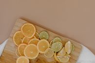 Top view of sliced with yellow lemons near oranges and green limes on wooden cutting board on white napkin on beige surface in light place