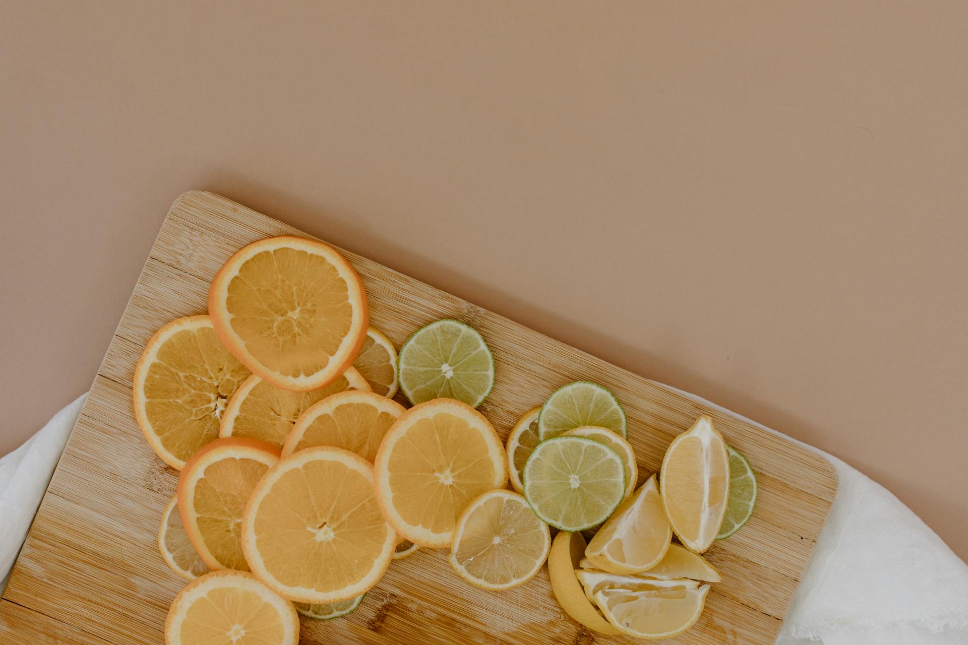 Top view of sliced with yellow lemons near oranges and green limes on wooden cutting board on white napkin on beige surface in light place