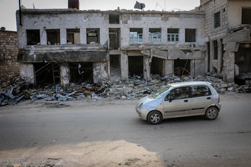 Automobile parked on road near old demolished house with broken windows and remains of building in poor district of town