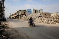 Active man riding motorcycle on empty straight roadway along destroyed buildings and piles of ruined houses in district of town