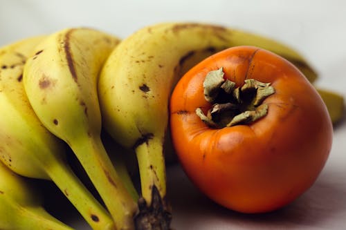 Free Persimmon Fruit Beside a Bunch of Bananas Stock Photo