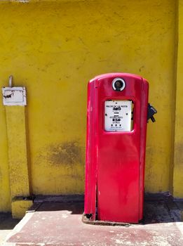 A classic red gas pump against a vibrant yellow wall in Catia La Mar, Venezuela.