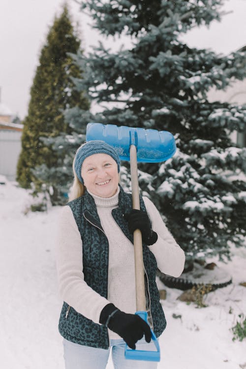 A Woman Holding a Shovel While Standing on the Snow Covered Ground Near the Tree