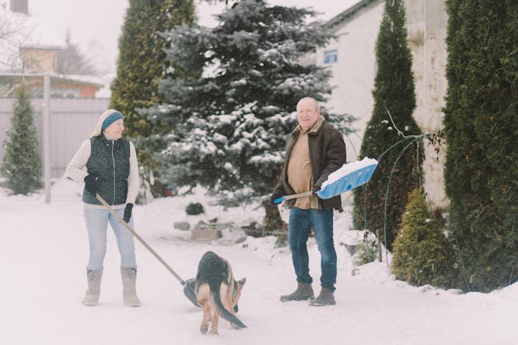 Couple Shoveling Snow With Dog