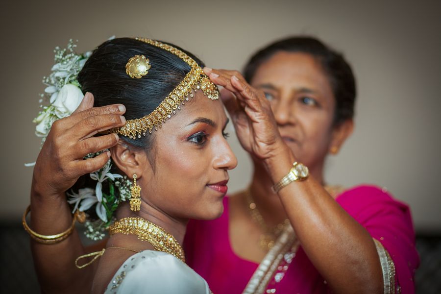 Adjusting a golden Kandyan accessory on a bride