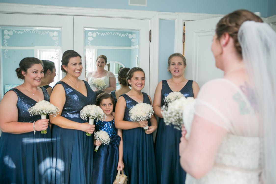 Positive bride standing in room with smiling bridesmaids on wedding day ...