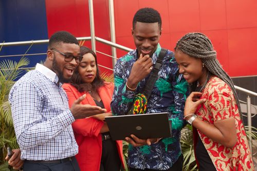 Free Four young adults collaborating on a project using a laptop outdoors, showcasing teamwork and diversity. Stock Photo