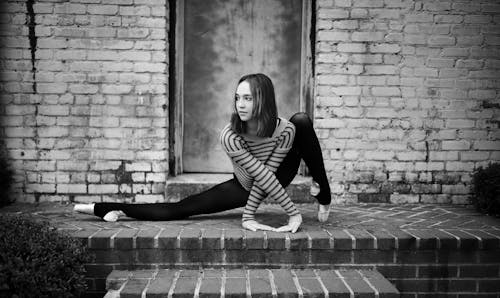 Free Black and white full length positive flexible female gymnast doing split and crossing arms gracefully outside shabby brick building and looking away Stock Photo