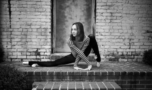 Free Black and white full length positive flexible female gymnast doing split and crossing arms gracefully outside shabby brick building and looking away Stock Photo