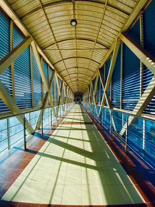 Free A modern, narrow passageway with metal railings and tiled floor casting reflections. Stock Photo