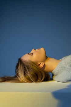 Portrait of a woman with blonde hair lying back with eyes closed against a blue background.