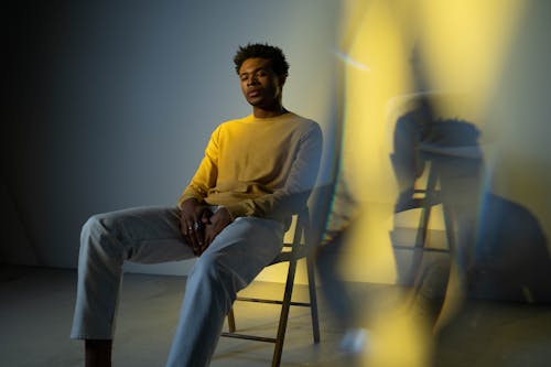 Man in Yellow Long Sleeve Shirt and Gray Pants Sitting on Chair