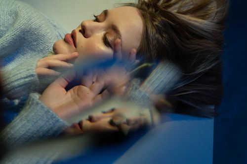 Free A serene woman in a gray sweater lies with a prism effect, creating an abstract reflection. Stock Photo