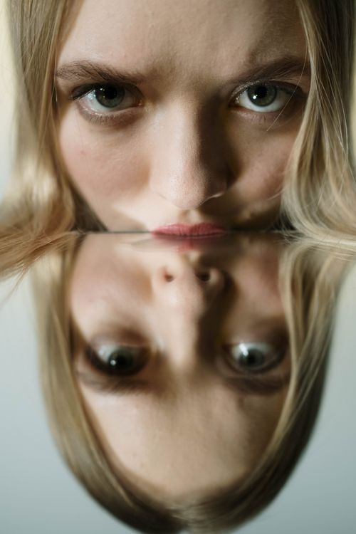 Free Close-up of a woman's face reflected in a mirror creating a symmetrical artistic composition. Stock Photo