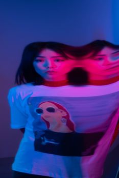 Artistic portrait of a woman wearing a graphic tee under a colorful light with prism distortion.