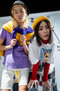 Two stylish teenagers showcasing colorful streetwear indoors, expressing modern fashion and youth culture.