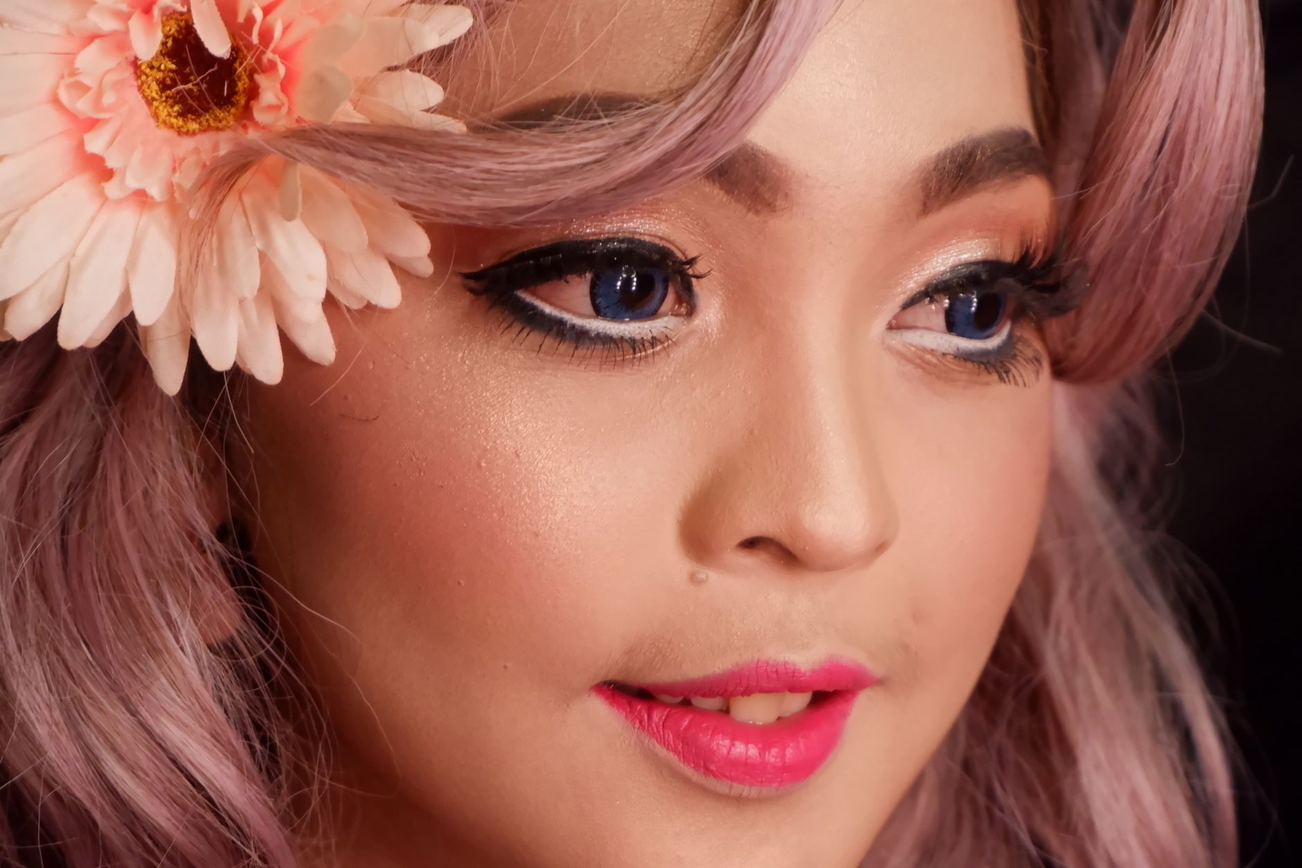 Detailed close-up of an Asian woman with floral accessory, highlighting makeup and vibrant features.