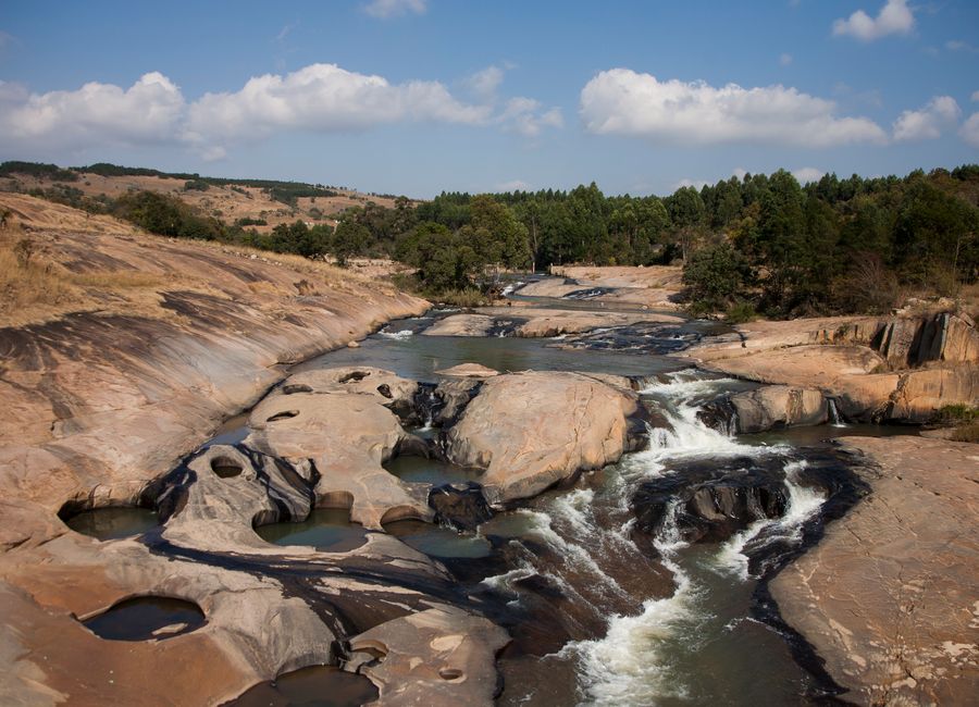 Stunning view of rocky cascades and trees along a river in Eswatini, showcasing natural beauty and tranquility.