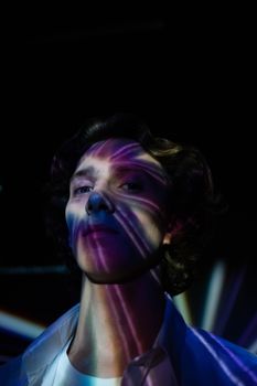 A surreal portrait of a man with colorful light effects casting patterns on his face in a dark setting.