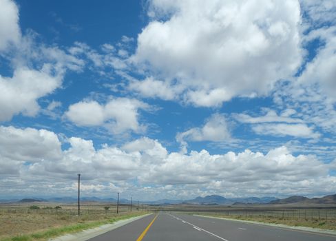Expansive open road stretching into horizon under bright blue sky with fluffy clouds.