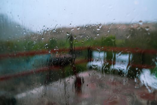 Close-up of raindrops on glass blurring an outdoor scene, capturing a rainy and moody atmosphere.