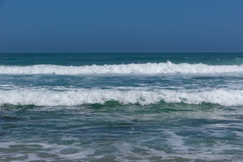 Free Serene ocean waves gently crashing on the shore under a clear blue sky, perfect for relaxation themes. Stock Photo