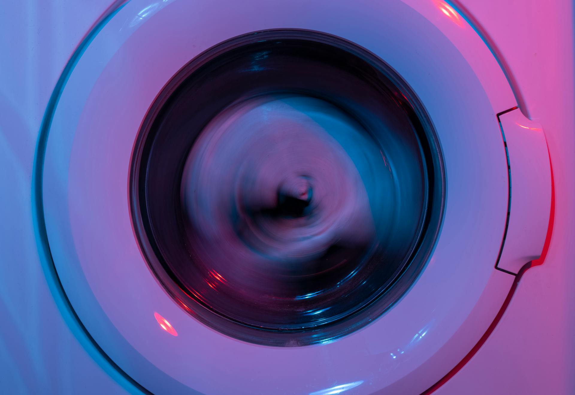 A washing machine spinning clothes under vibrant purple and blue lights.