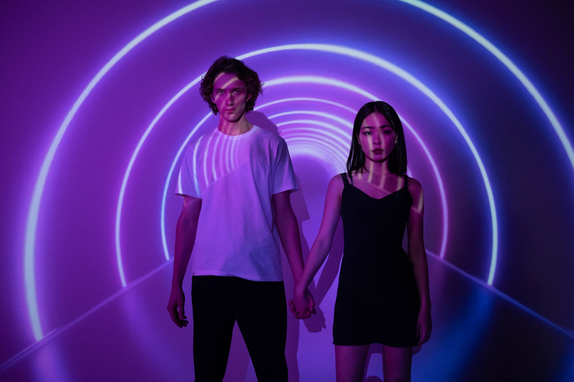 Young couple holding hands in a vibrant purple-lit tunnel with abstract circle patterns.