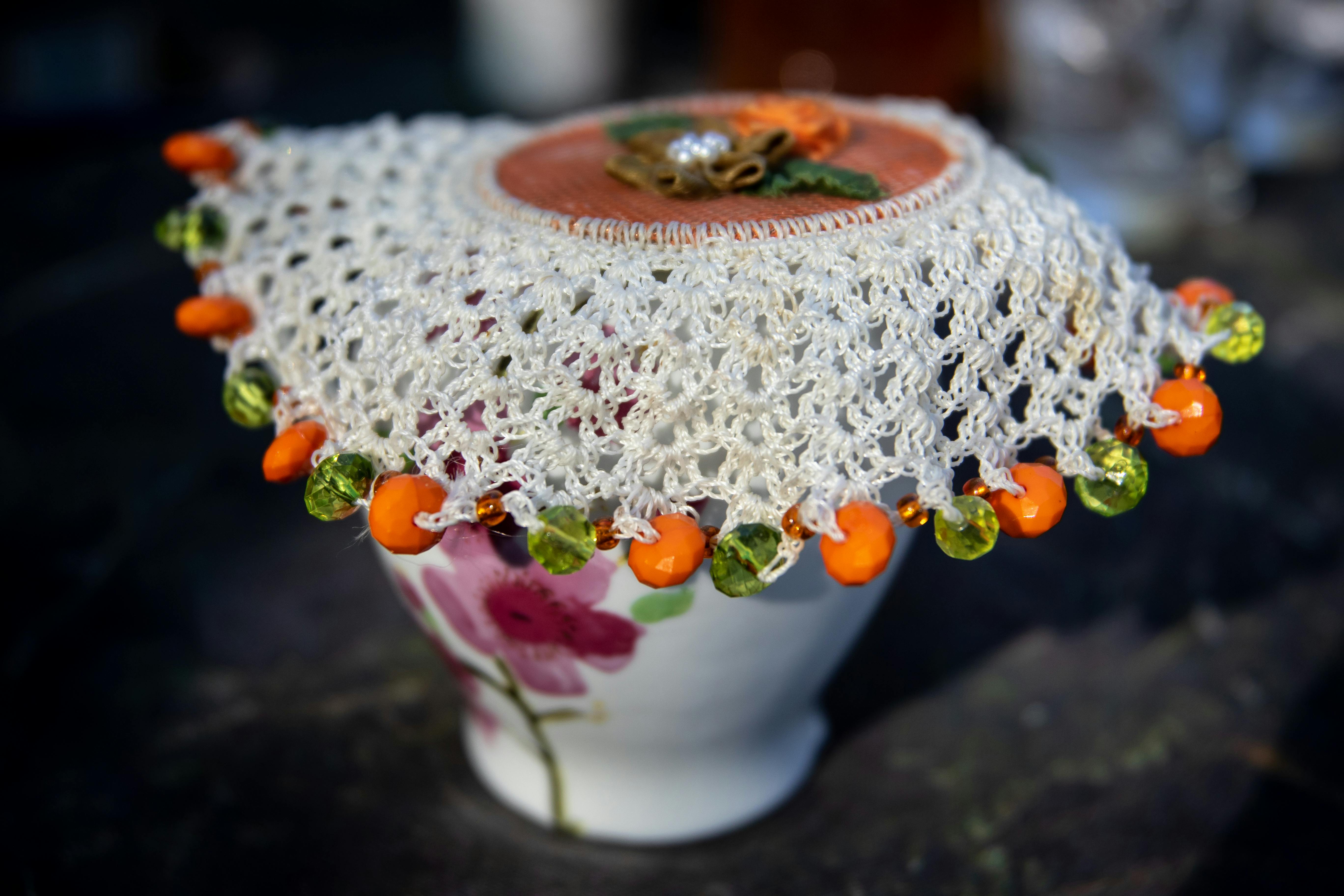 A handmade crochet doily with beads beautifully adorns a floral teacup, capturing a cozy home decor vibe.