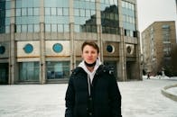 Young man standing near modern building and smiling at camera in winter
