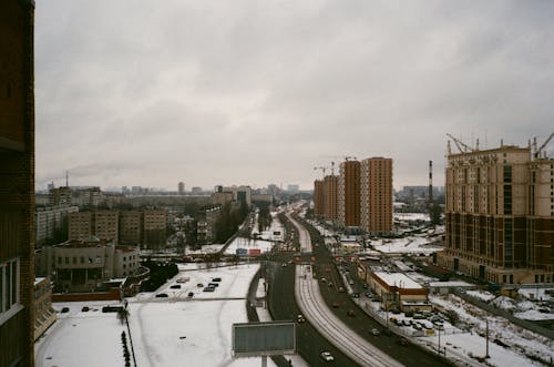 Modern apartment city district with snowy streets and buildings under construction on gloomy overcast winter day