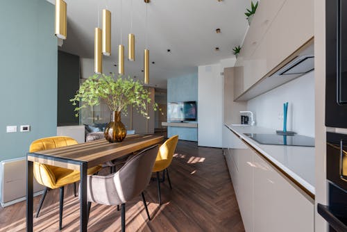 Interior of light modern kitchen with green flowers in vase placed on table near cabinets in light apartment with hanging lamps