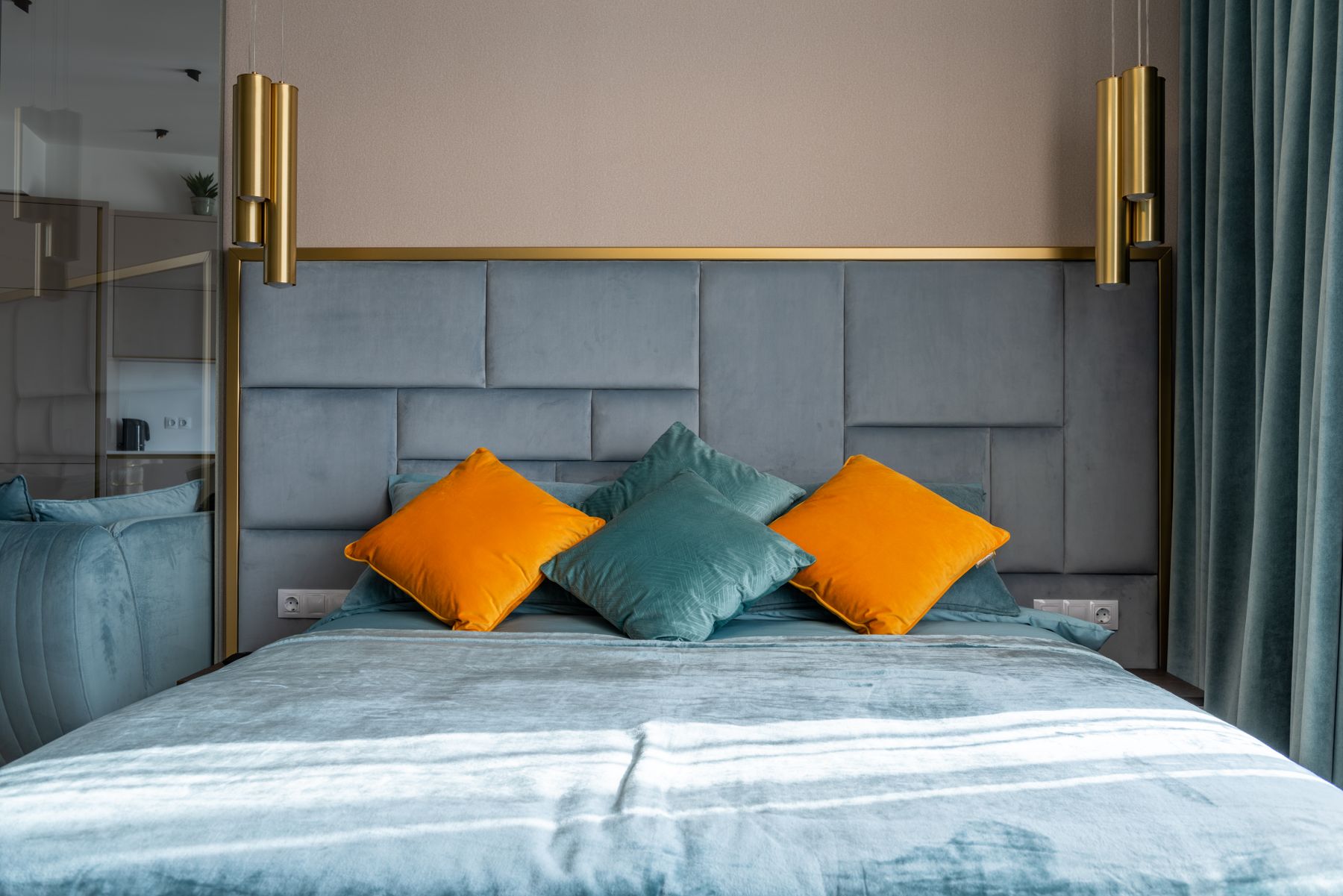 Contemporary bedroom with teal bedding, colorful cushions, warm headboard and hanging pendant lights