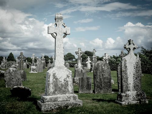 Free A serene cemetery scene with weathered Celtic cross gravestones under a cloudy sky. Stock Photo