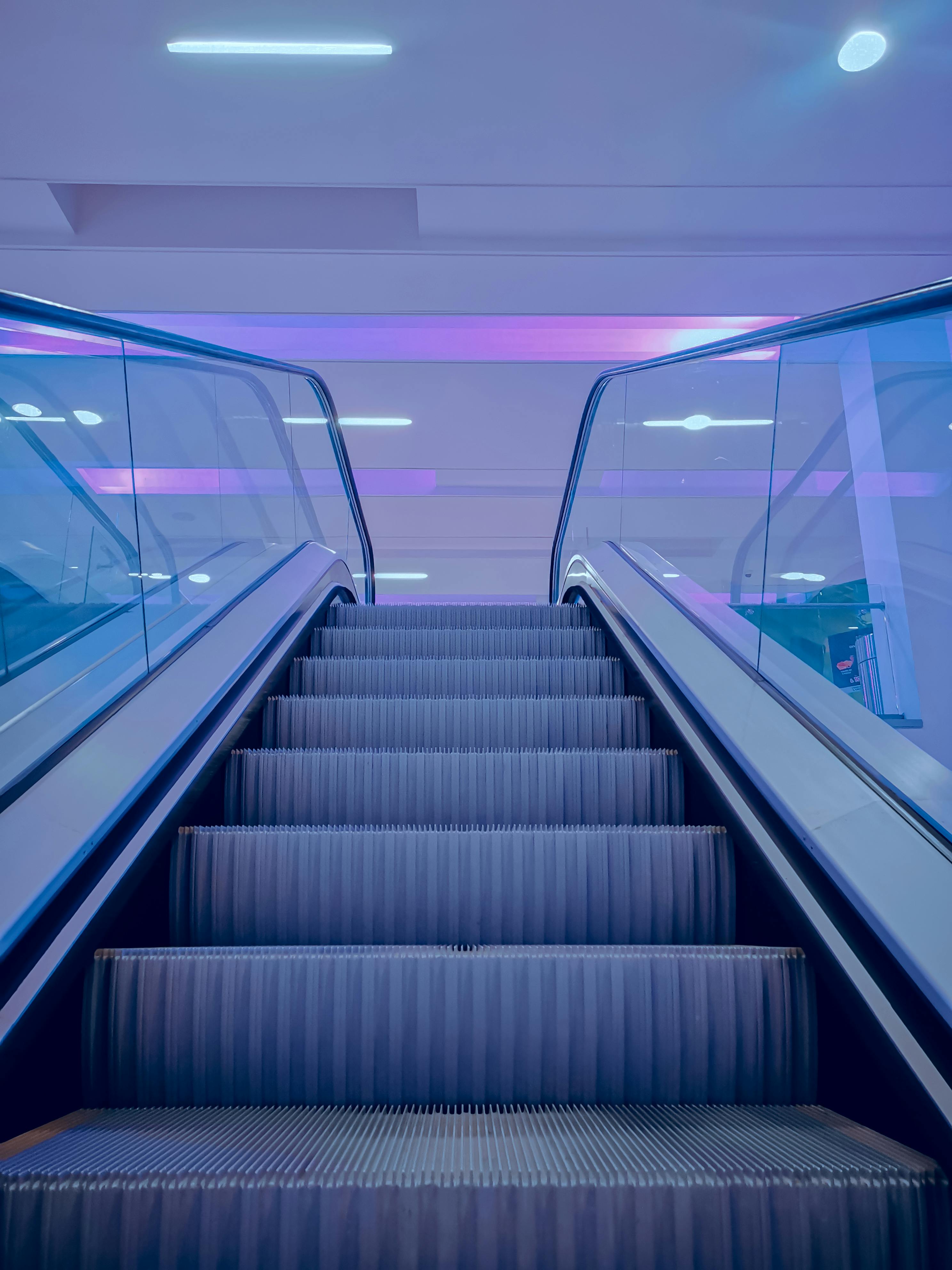 Free Indoor escalator under neon lighting creating a futuristic ambiance in a shopping mall. Stock Photo