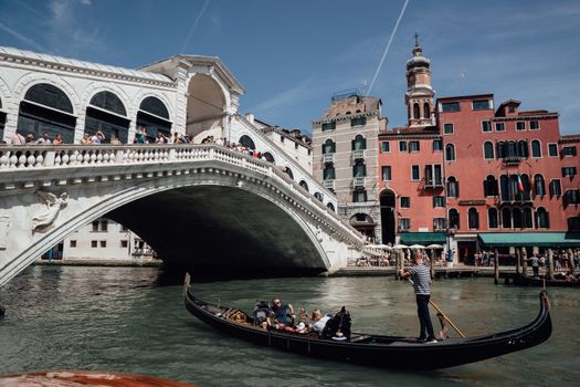 Travelers floating on gondola on Grand canal near famous bridge among aged residential buildings in Venice during vacations in Italy