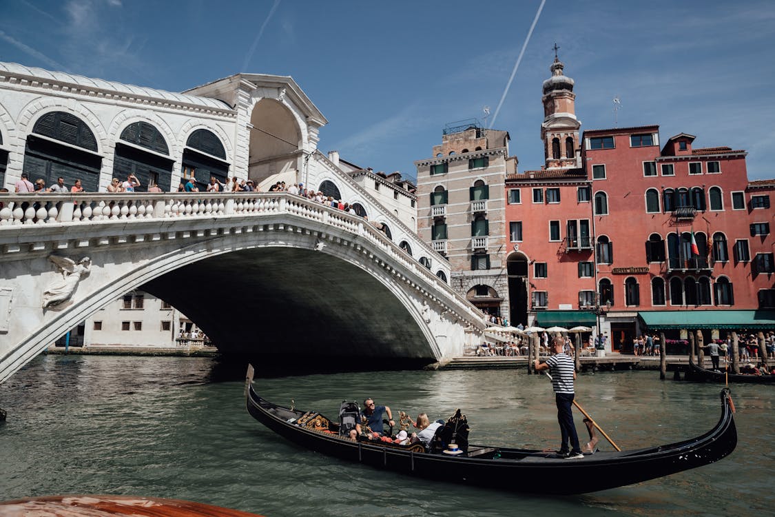 Travelers floating on gondola on Grand canal near famous bridge among aged residential buildings in Venice during vacations in Italy