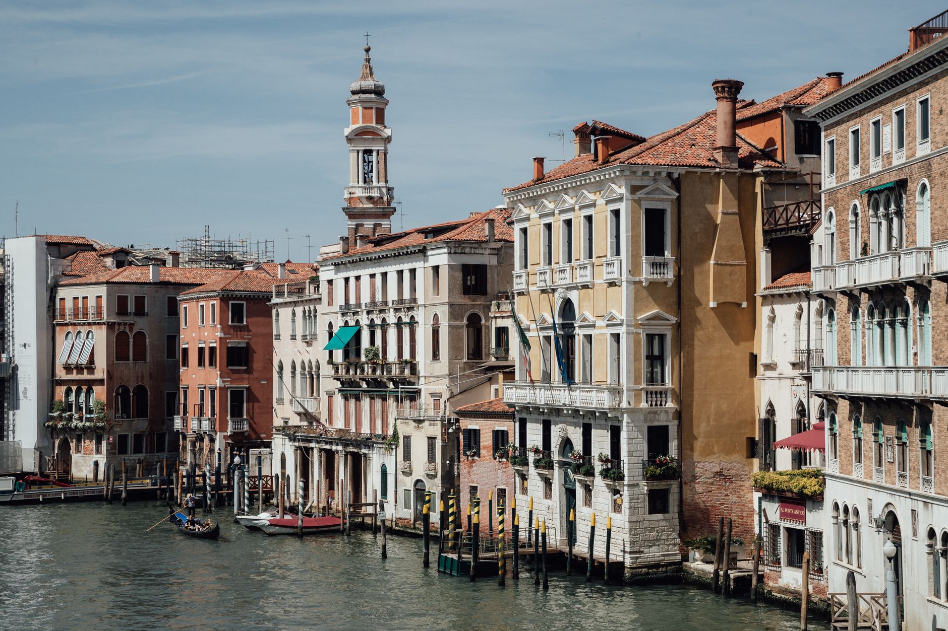 Exterior of old residential houses and tower located along famous Grand canal with gondolas in water of Venice Italy